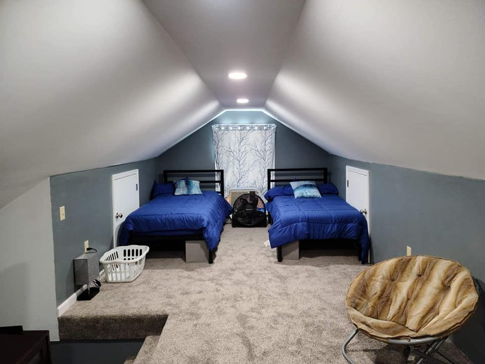 A bedroom with two beds and a chair in the attic.