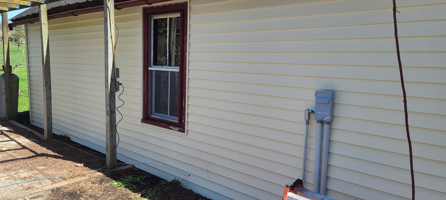 A white house with a red window and a ladder on the side of it.