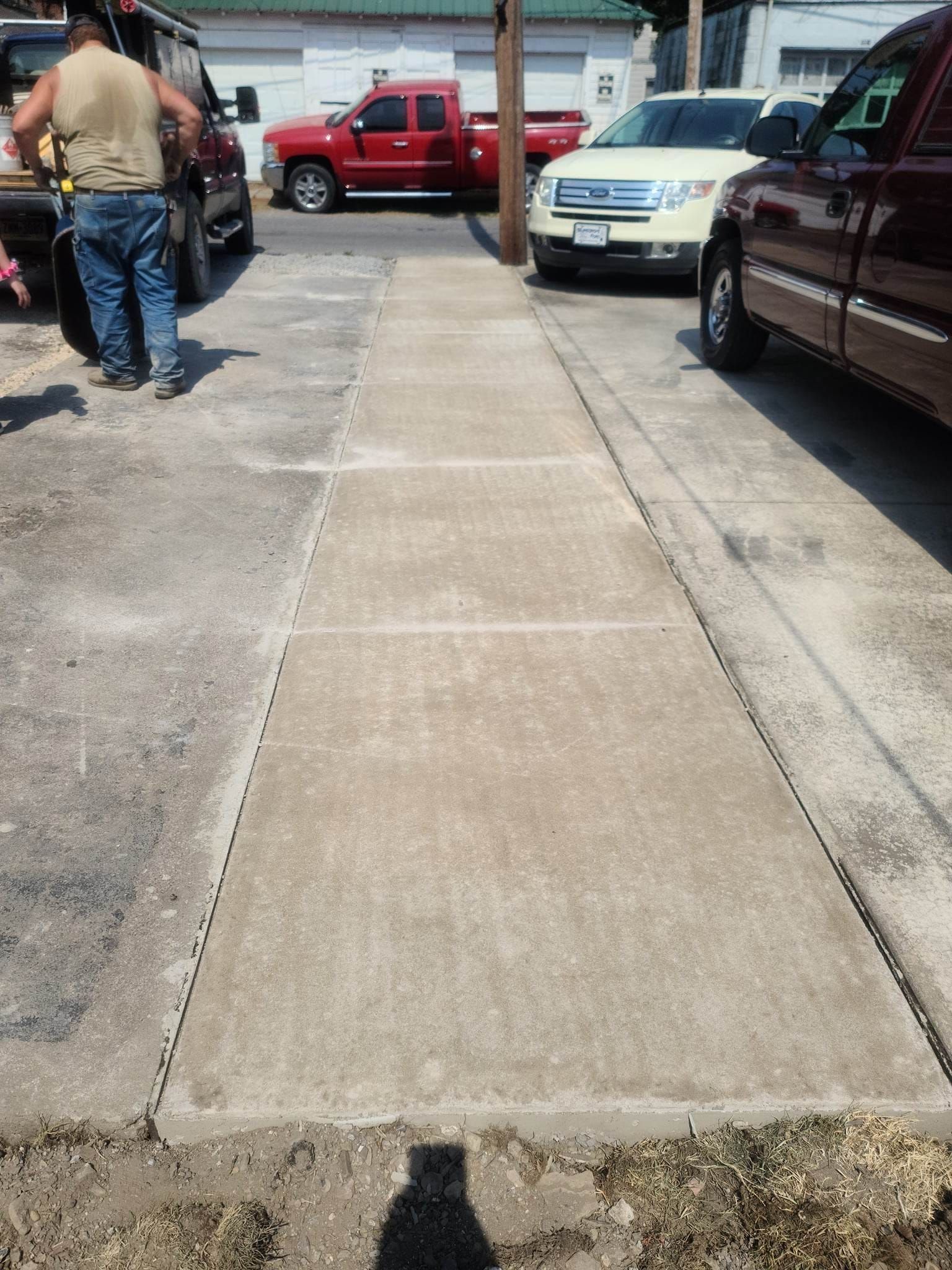 A man is walking down a sidewalk next to a parking lot filled with cars.