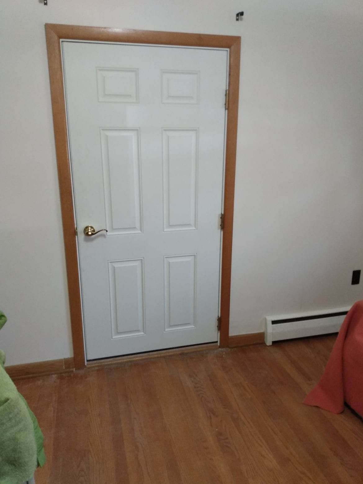 A white door with a wooden frame is in a room with hardwood floors.