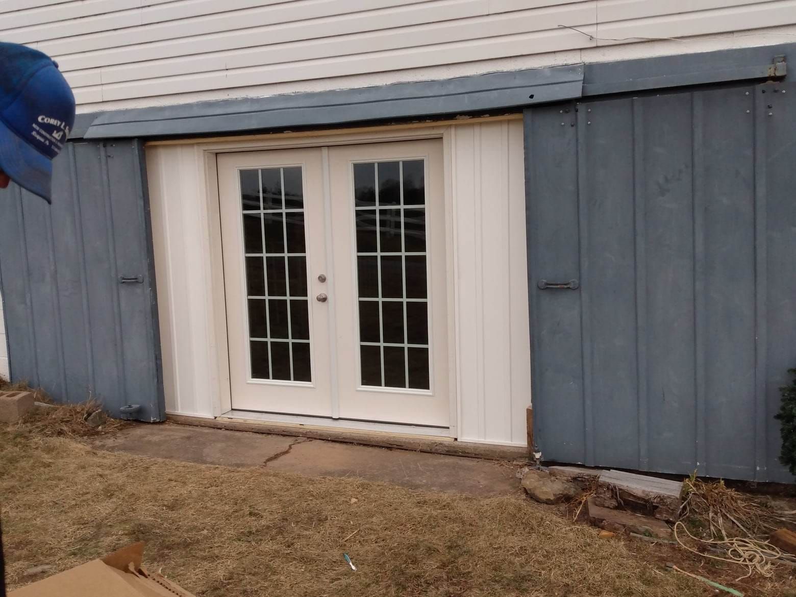 A man wearing a blue hat is standing in front of a white door
