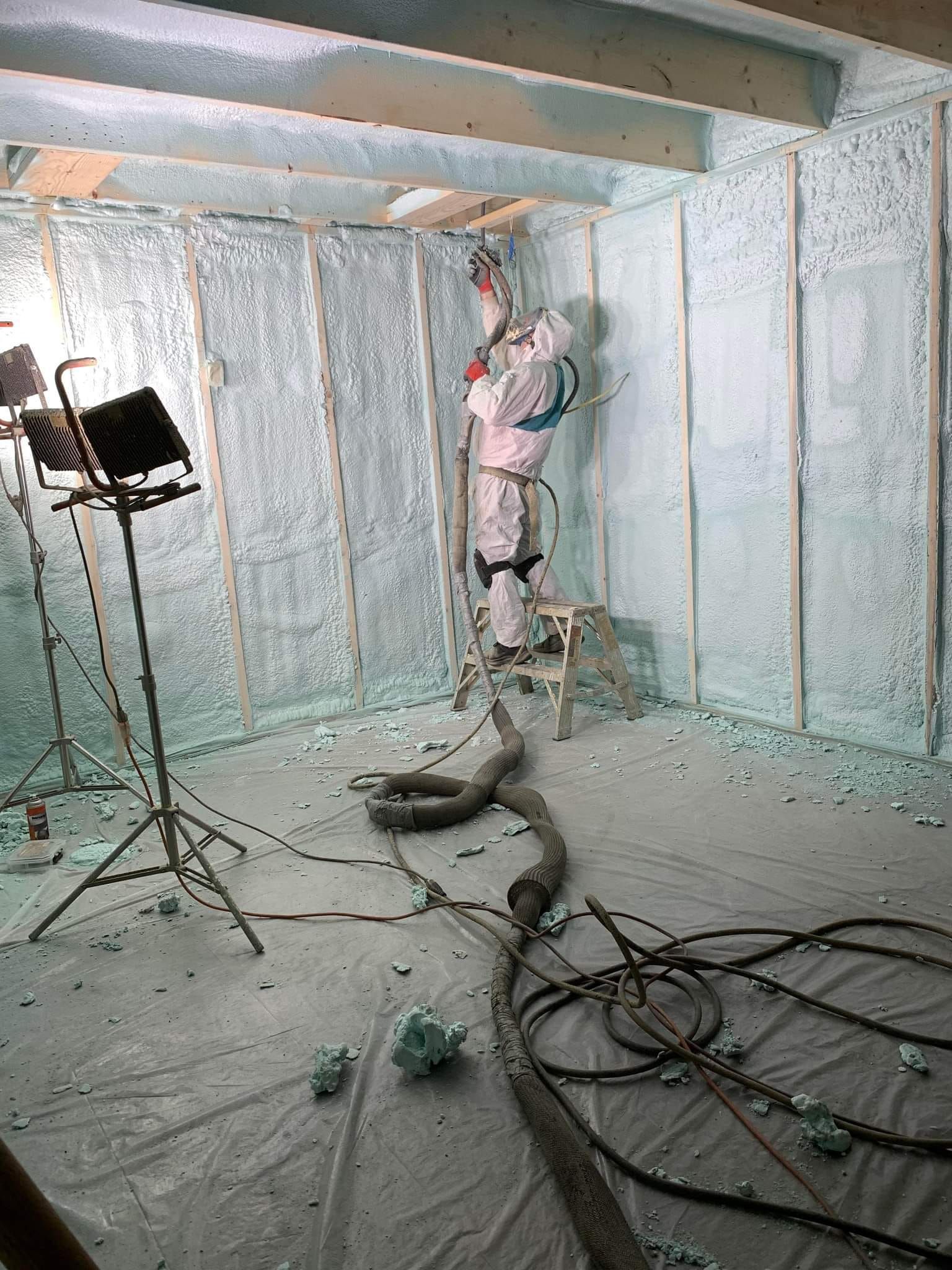 A man is spraying foam on a wall in a room.