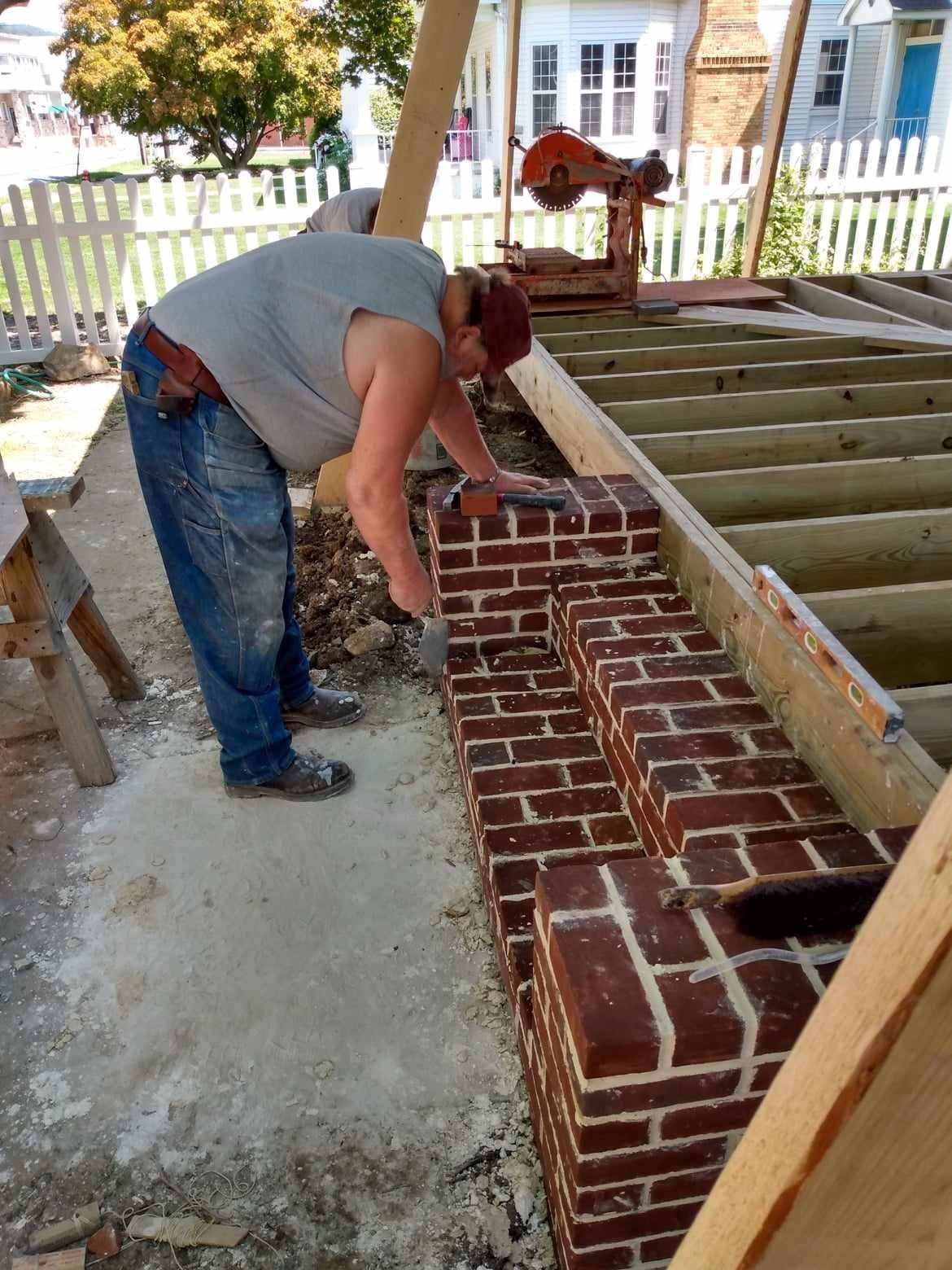 A man is laying bricks on a wooden deck