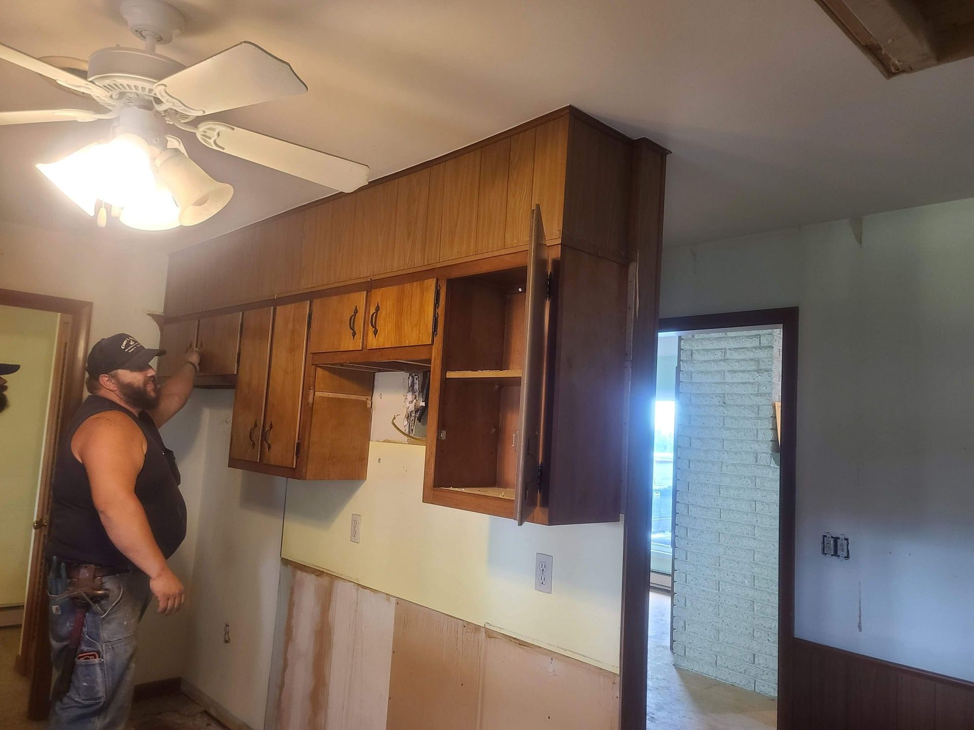 A man is standing in a kitchen under a ceiling fan.