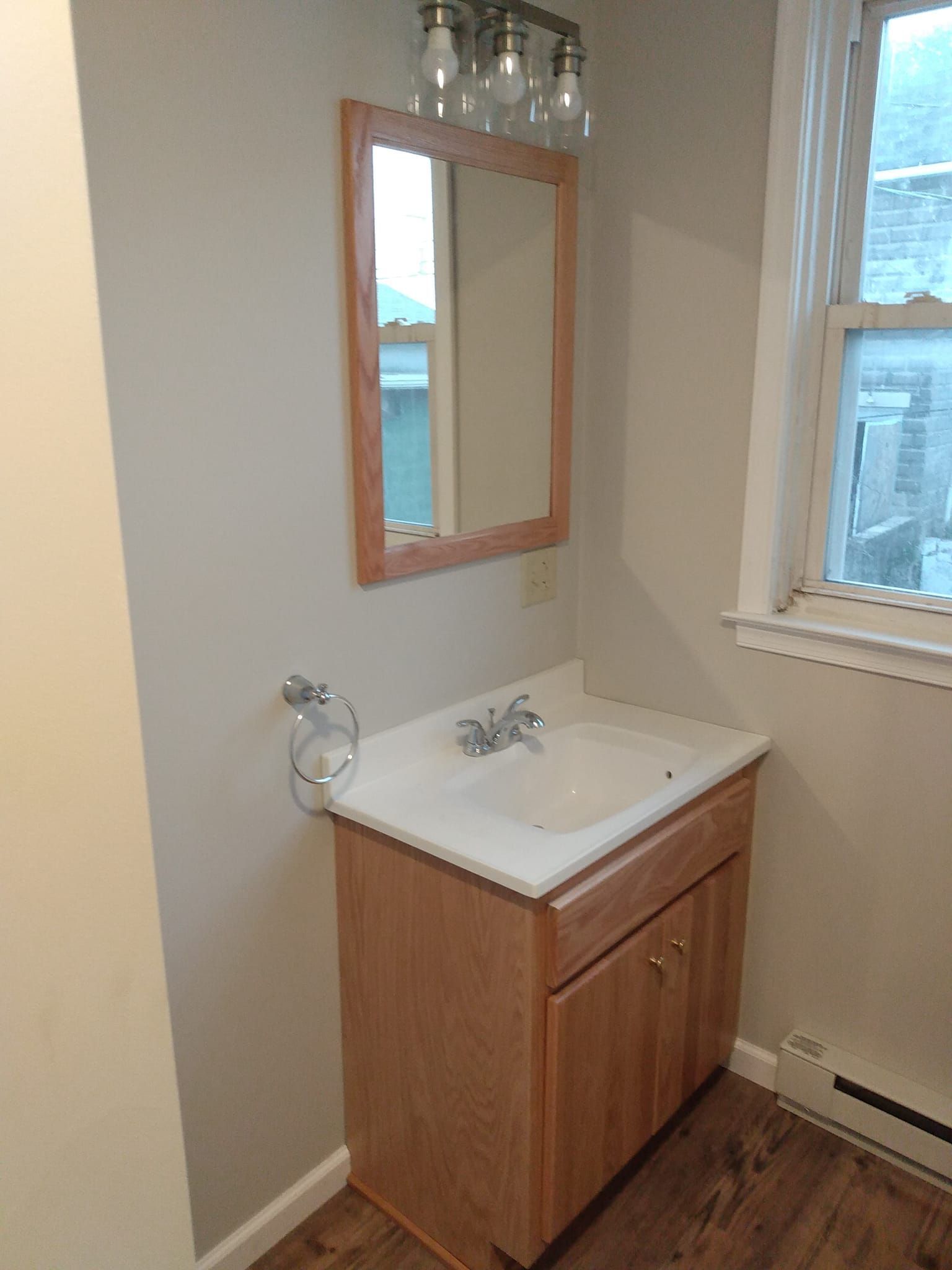 A bathroom with a sink , mirror and window.