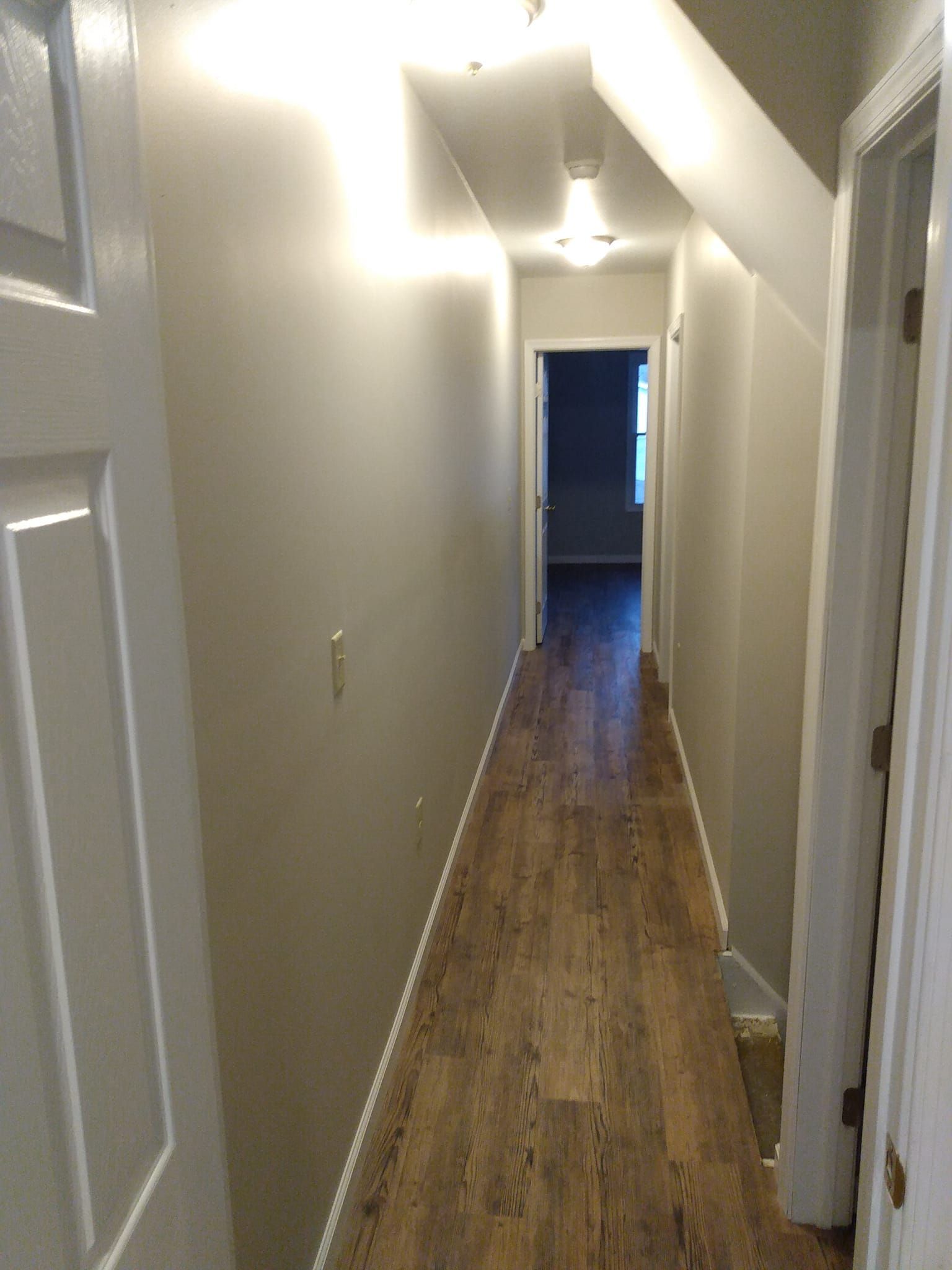 A long hallway with hardwood floors and white walls leading to a bedroom.