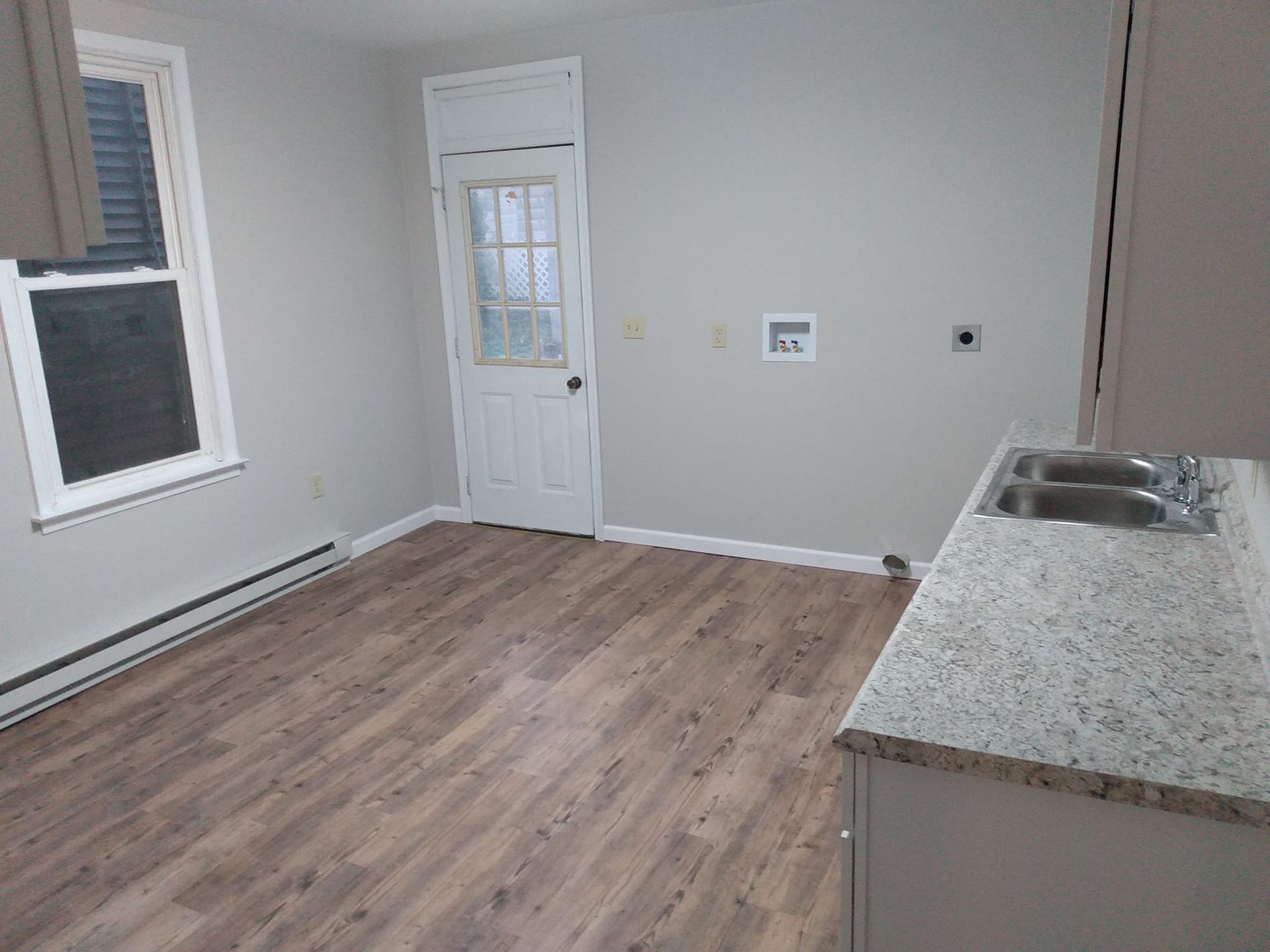 An empty room with hardwood floors , a sink , and a window.