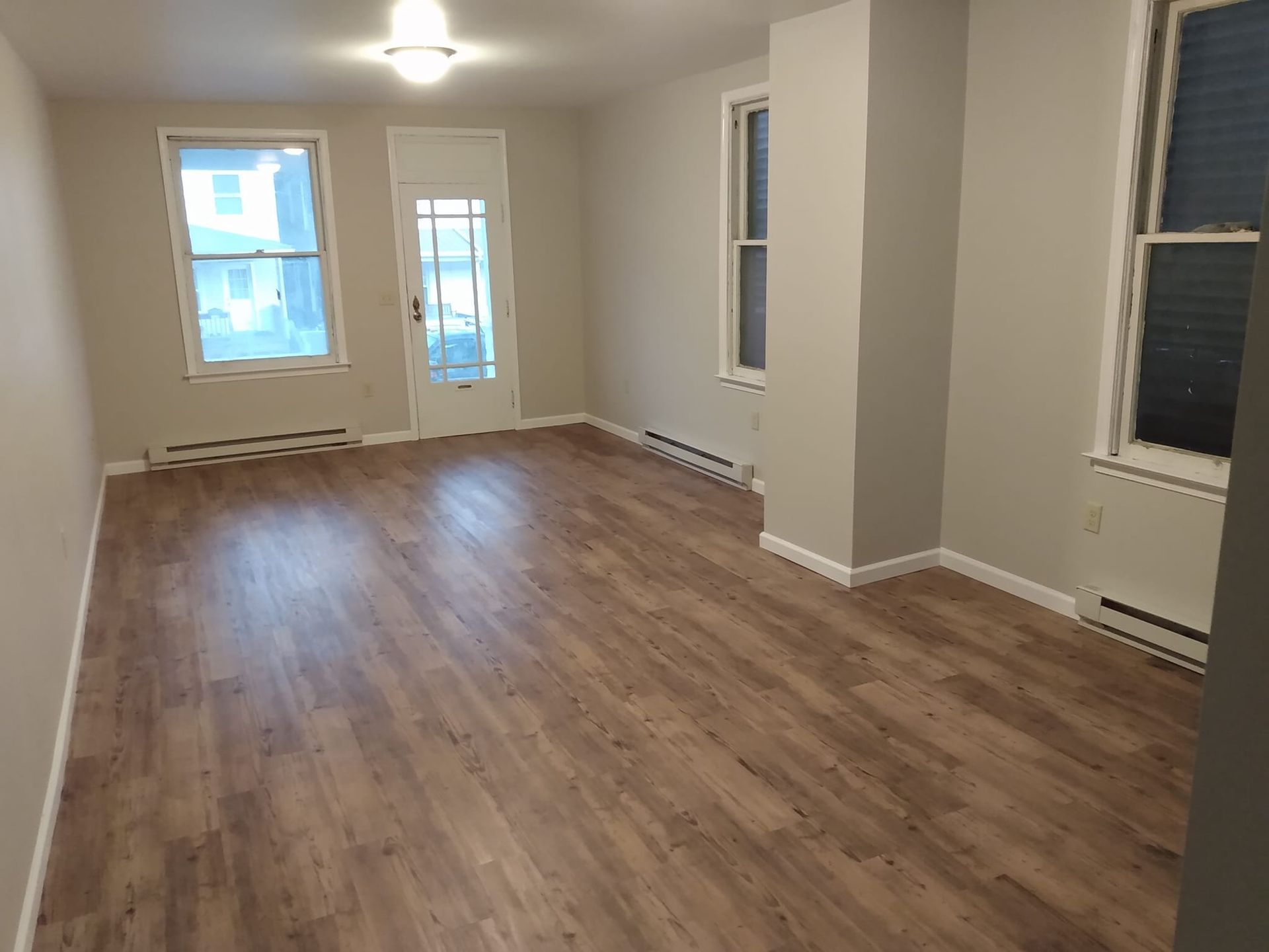 An empty living room with hardwood floors and two windows.