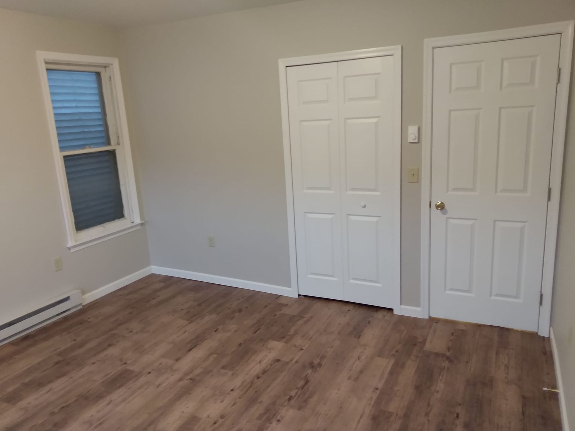 An empty bedroom with hardwood floors and white doors.
