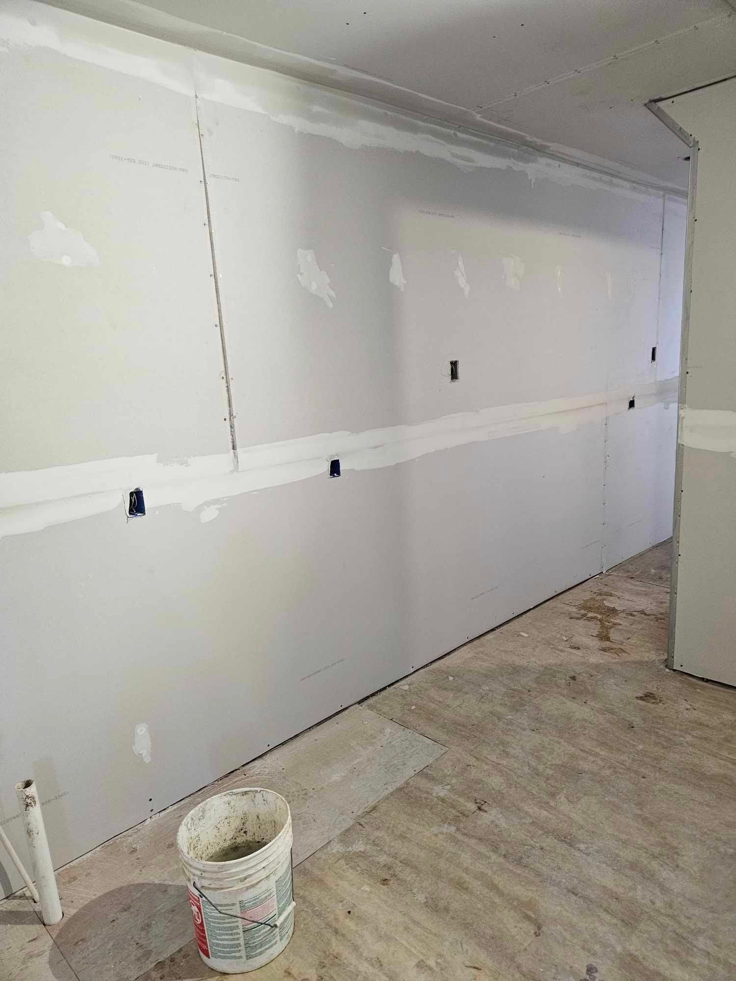 A bucket of paint is sitting on the floor in front of a wall.