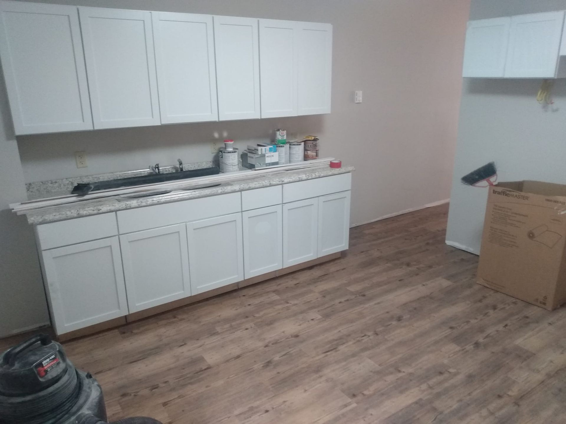 A kitchen with white cabinets and wooden floors is being remodeled.