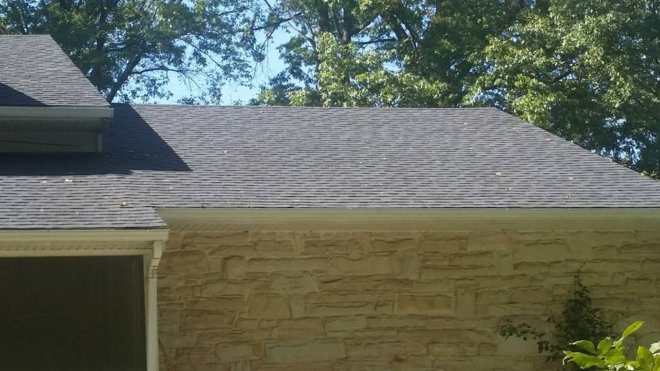 A brick house with a black roof and trees in the background.