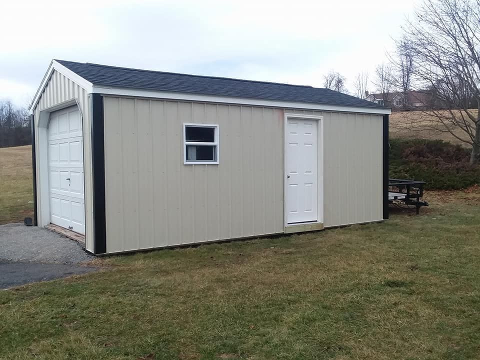 A shed with a garage door and a window is sitting in the middle of a grassy field.