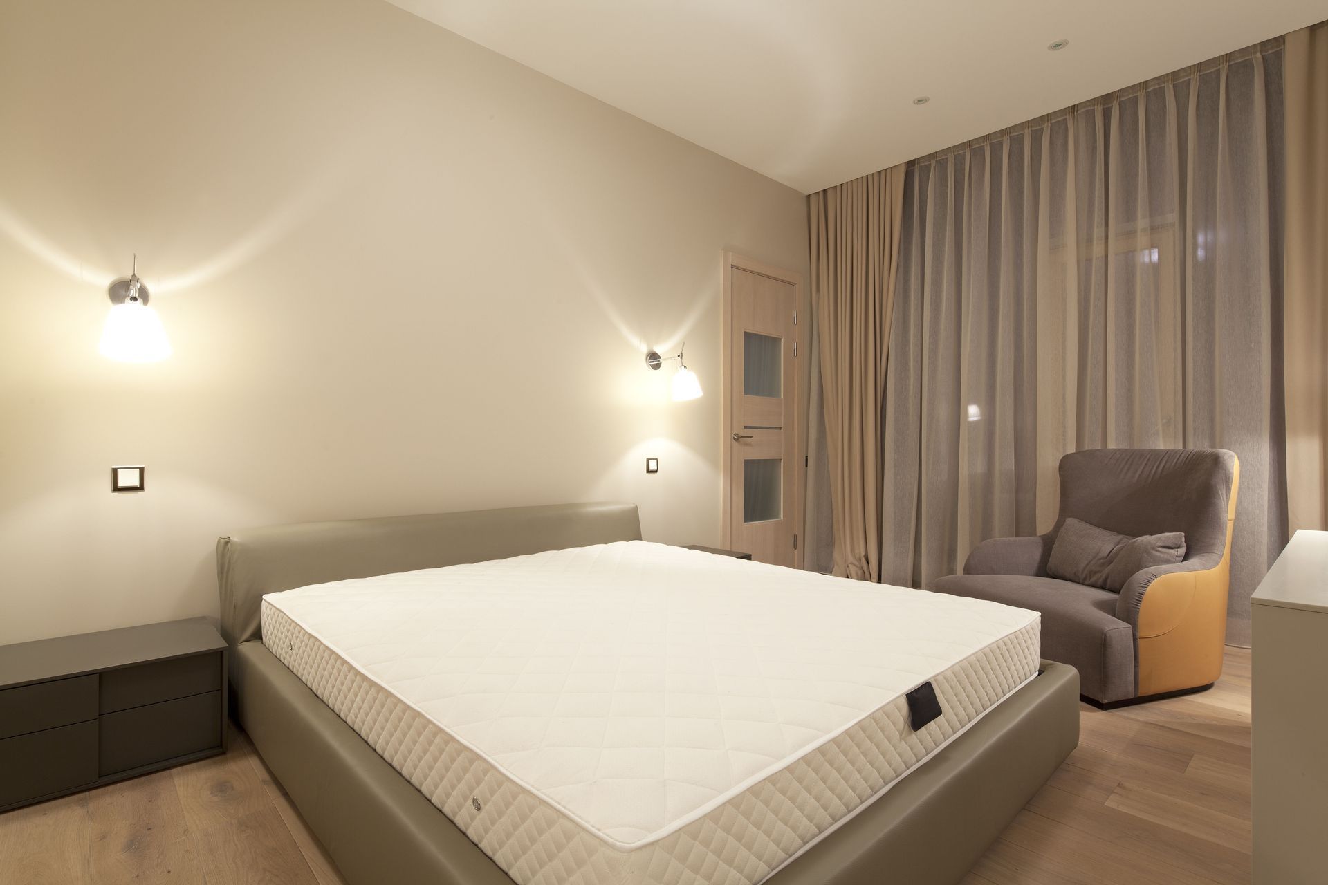 Bedroom with a bed, two sconces, armchair, and curtains; neutral colors.