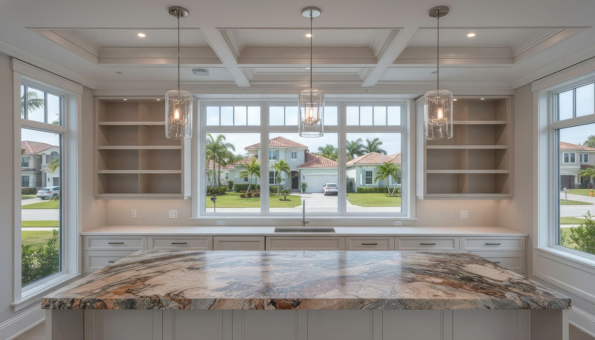 Kitchen with large granite island, built-in shelves, three pendant lights, and large window overlooking neighborhood