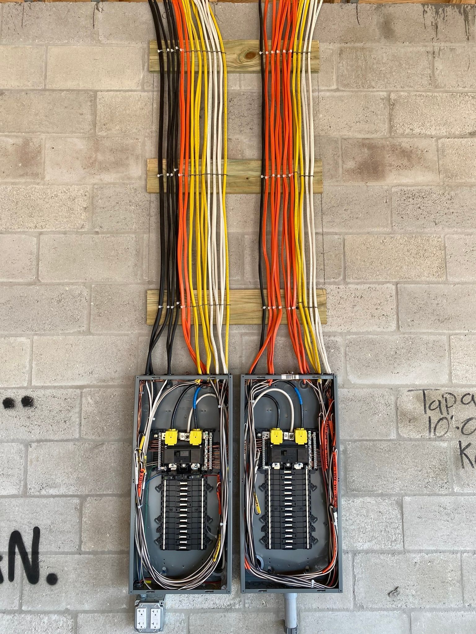 Two electrical panels with colored wires on a cinder block wall.