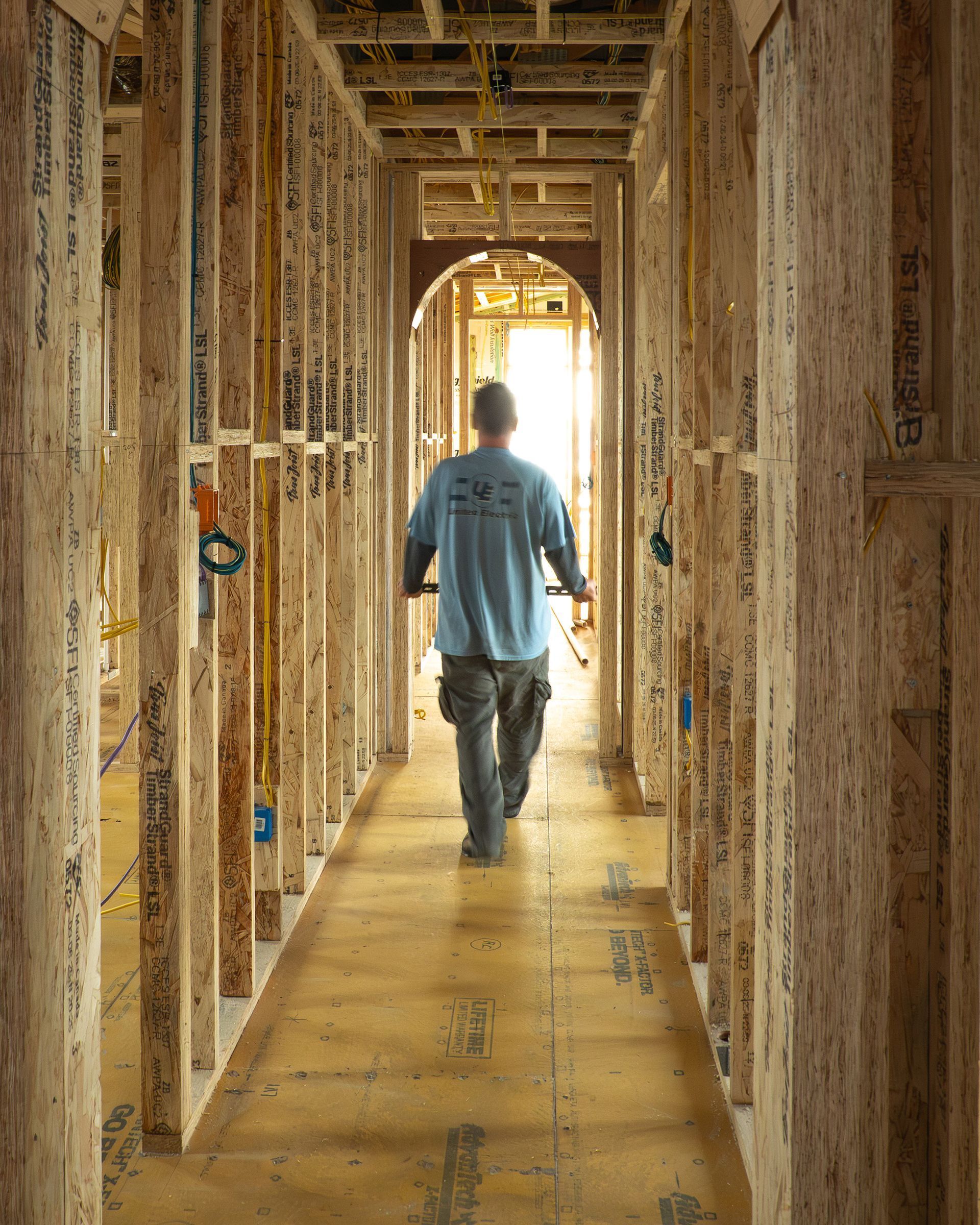 Construction worker walking down a hallway framed with wooden studs.