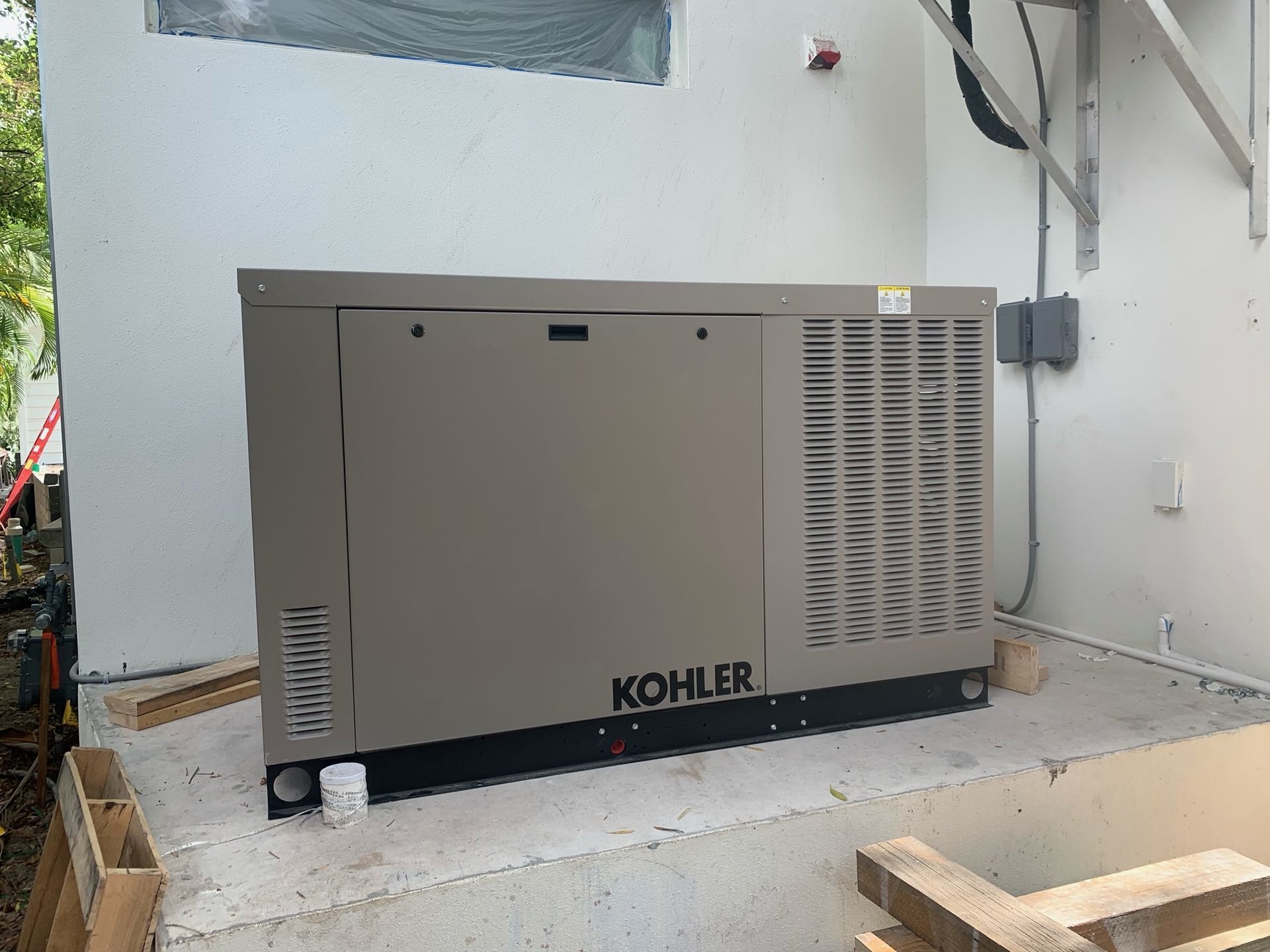 A large, tan Kohler generator installed on a concrete pad next to a white building.