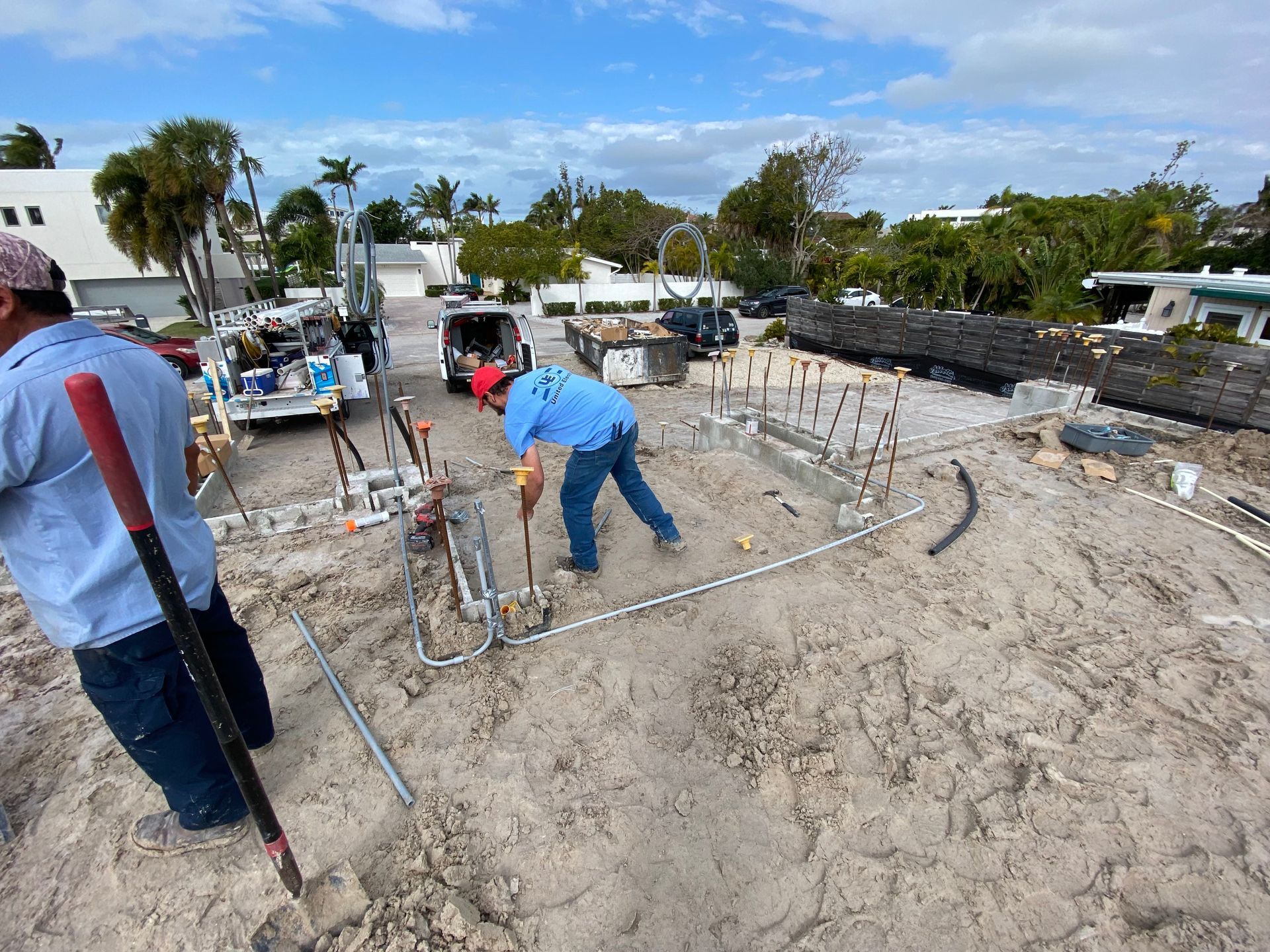 Construction workers installing pipes on a sandy lot under a bright blue sky.