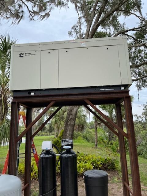 Cream-colored Cummins generator on a steel frame, outdoors. Trees and equipment are in the background.