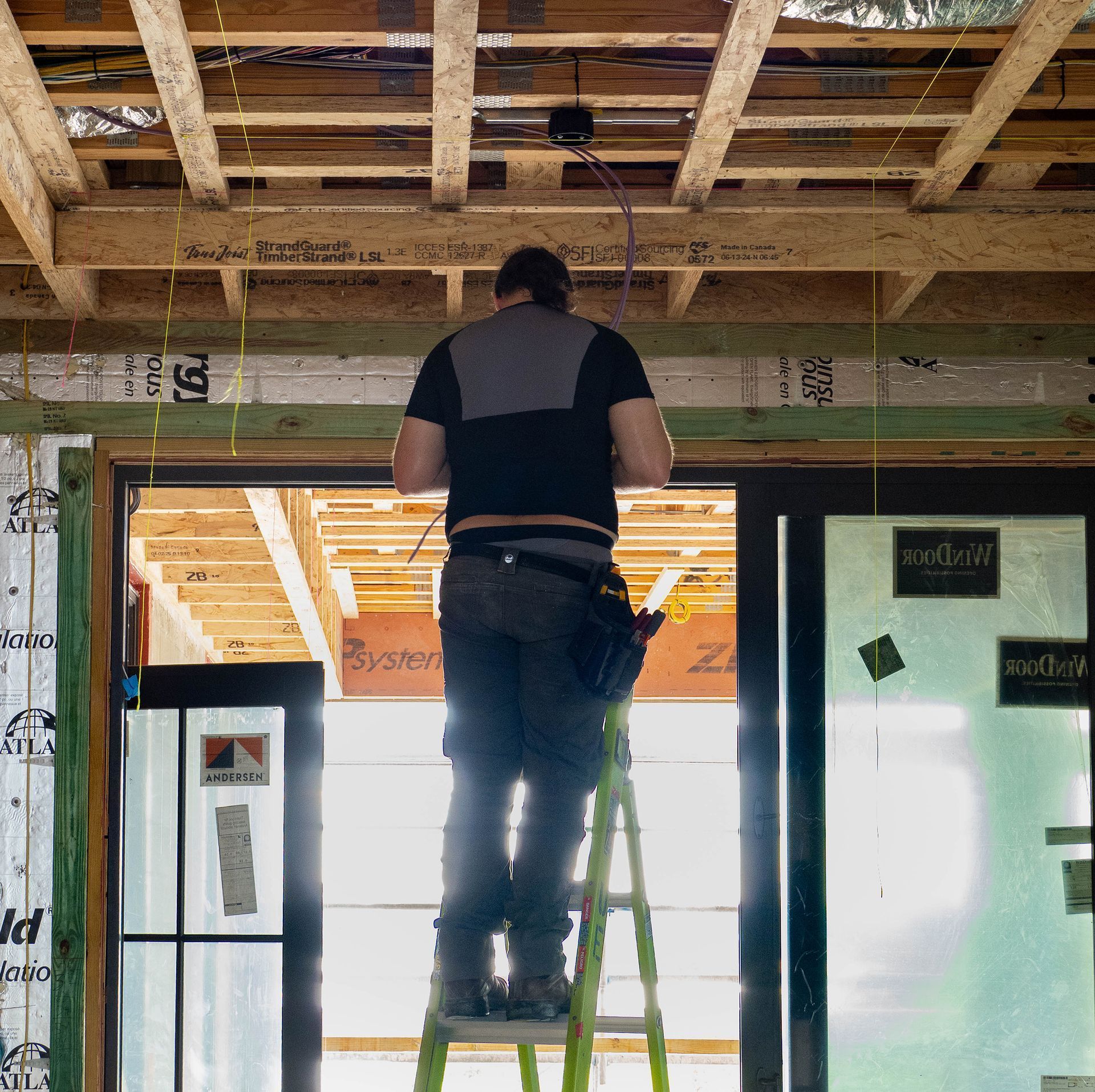 A person on a ladder installs electrical wiring in a building under construction.
