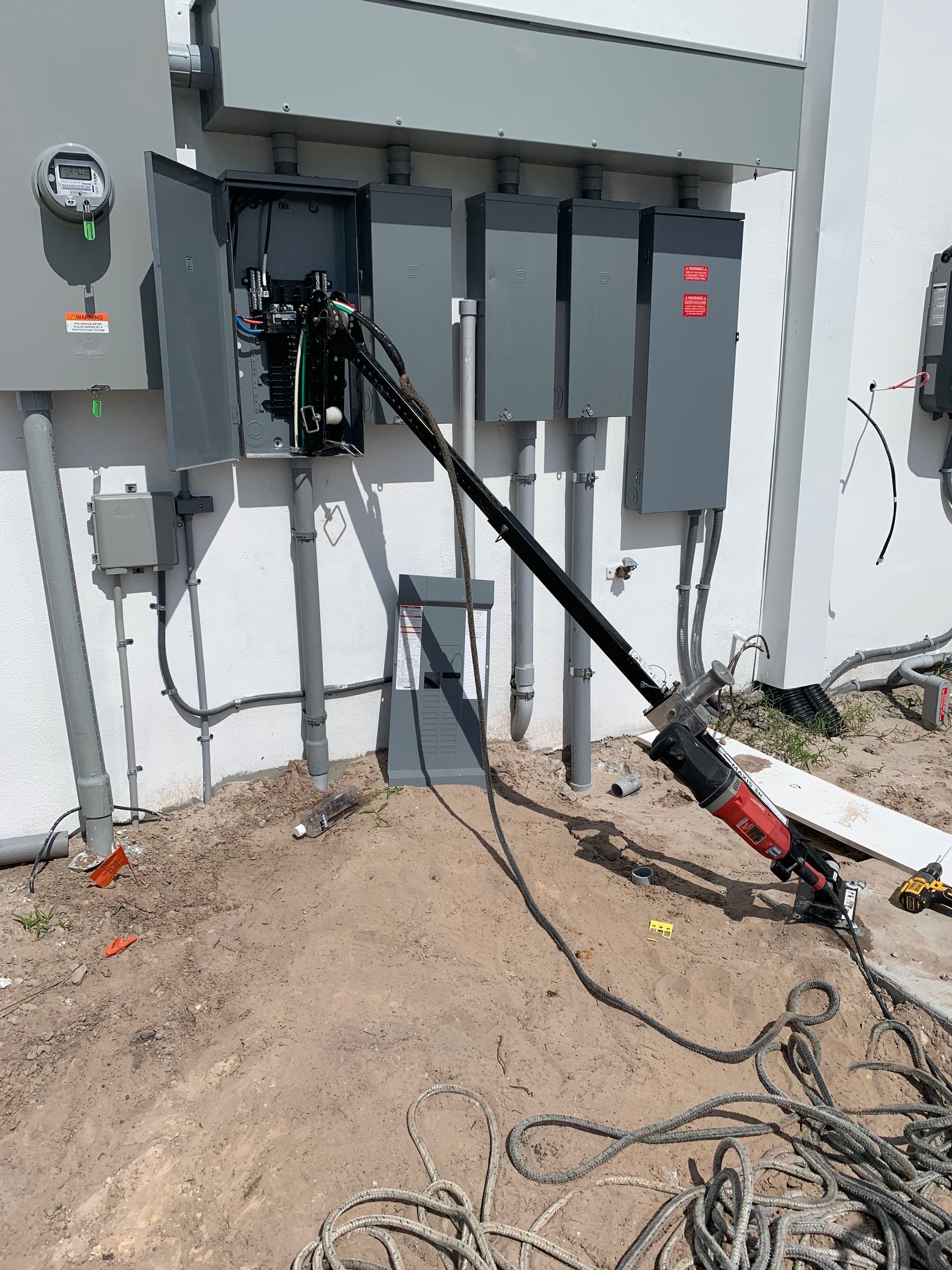 Electrical panel installation on a white building exterior; black cables and gray conduits.