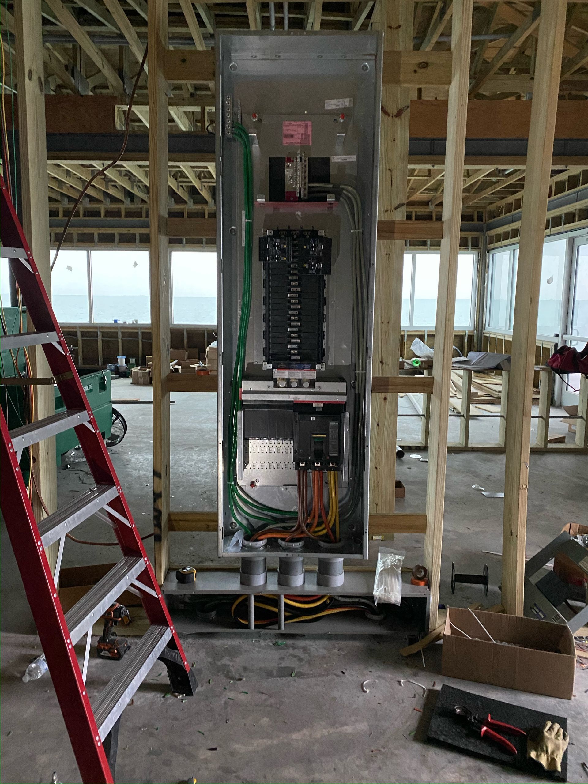 Electrical panel installed in a framed wall of a new construction home; a red ladder is next to it.