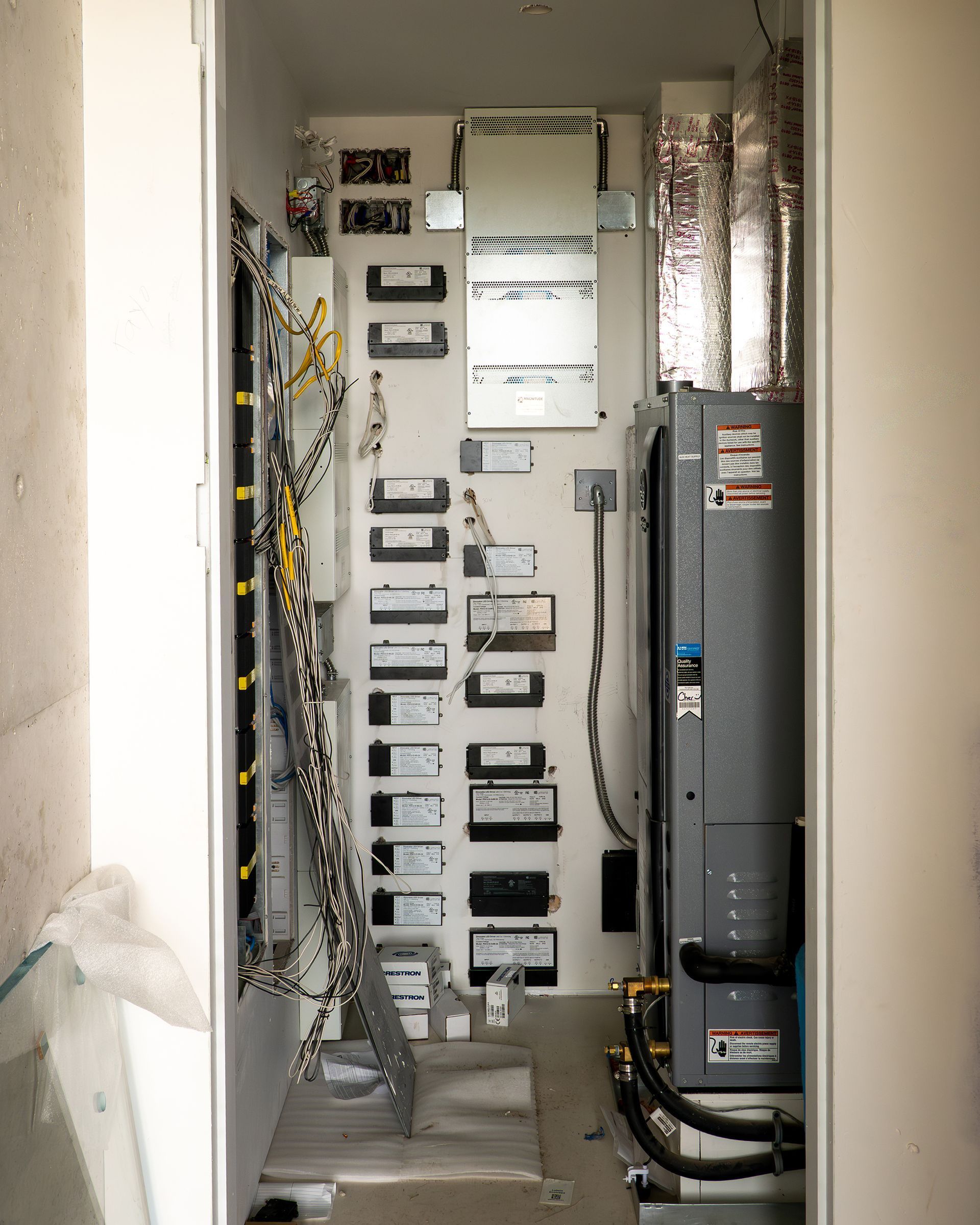 Electrical panel and HVAC unit in a narrow utility closet. Wires and components are visible.