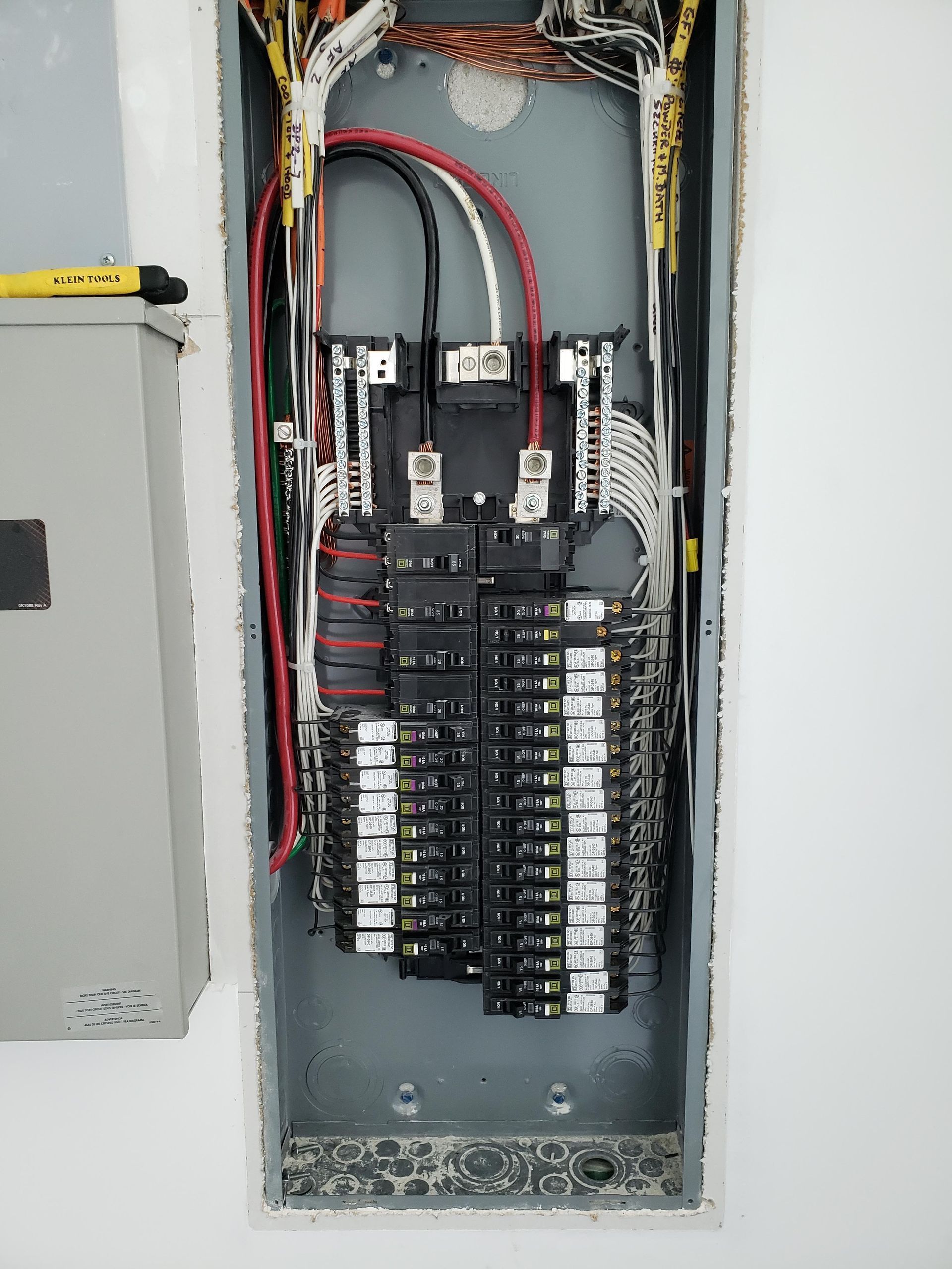 Electrical panel with wires and circuit breakers. Gray metal box set in a wall.