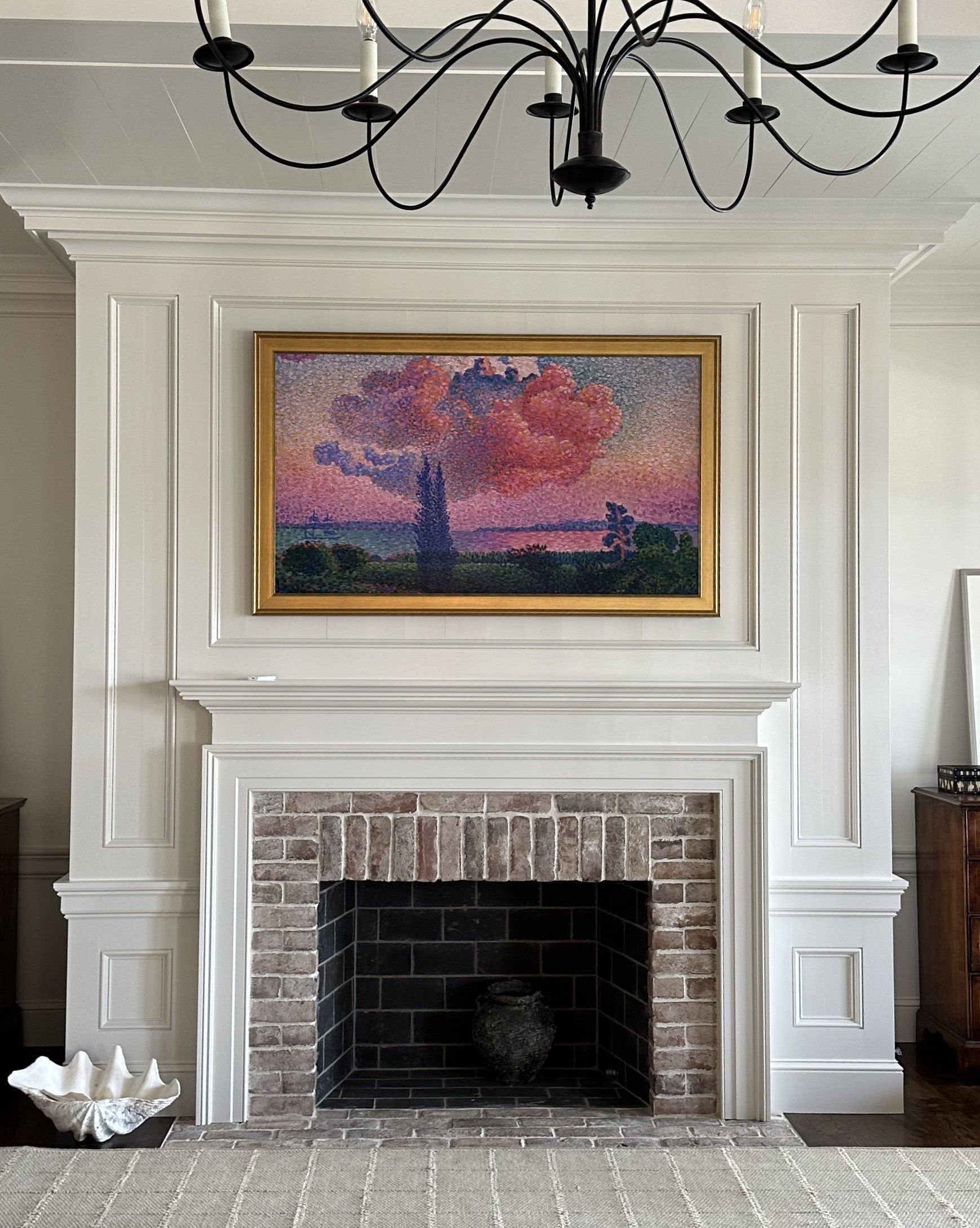 Fireplace with a brick surround, white mantel, and a colorful framed painting above it.