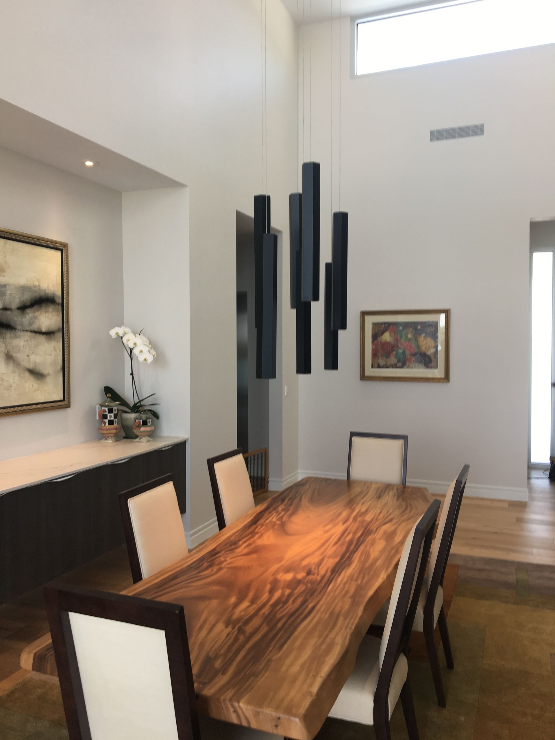 Dining room with a wooden table, chairs, art, and a black pendant light fixture.