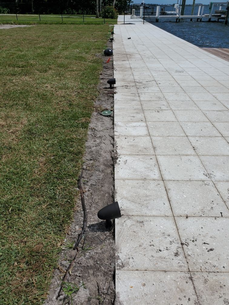 Sidewalk bordering a grassy area, with landscape lighting along the edge, next to water.