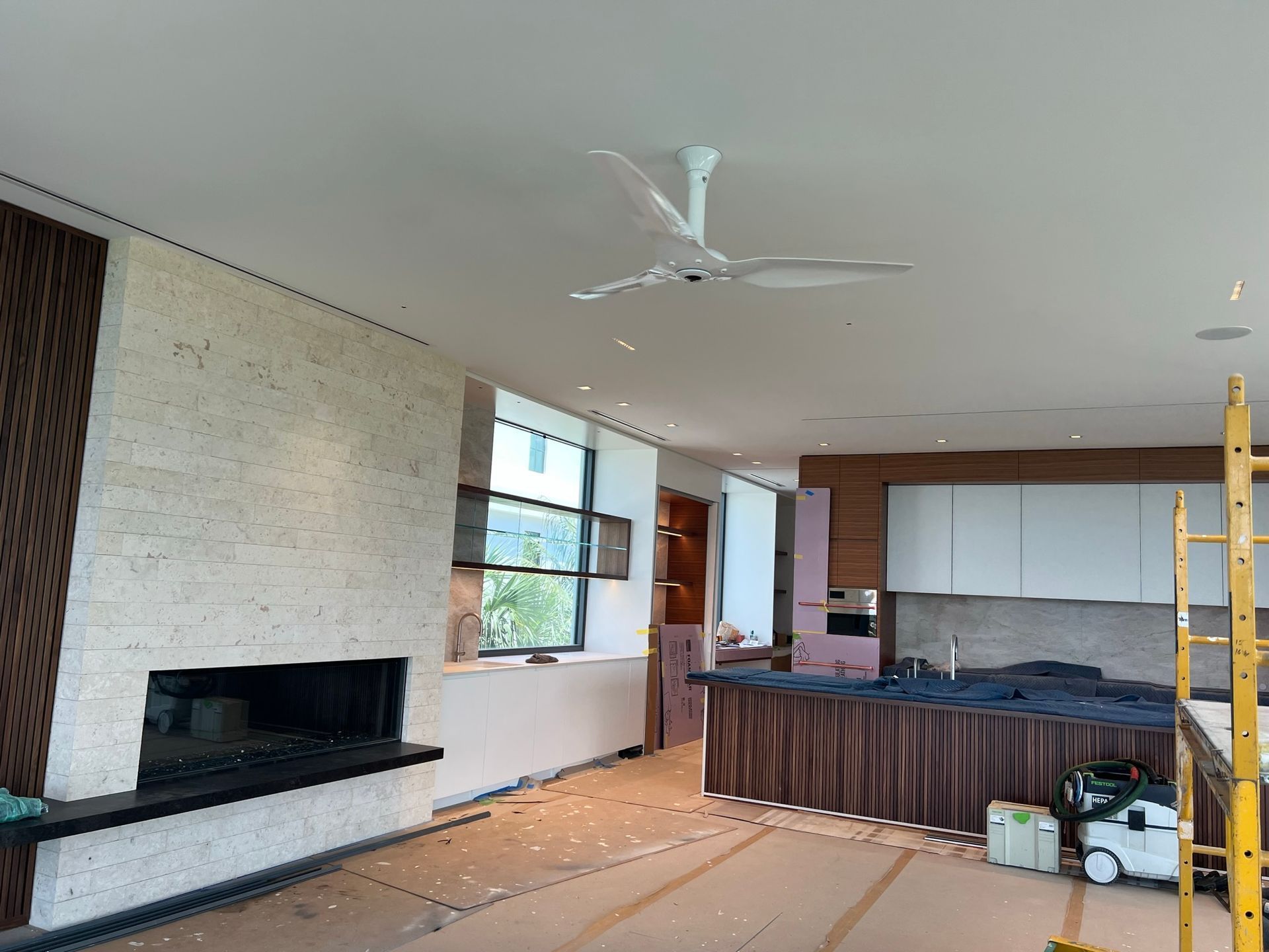 Interior view of a room under construction with a fireplace, kitchen cabinets, and a ceiling fan.