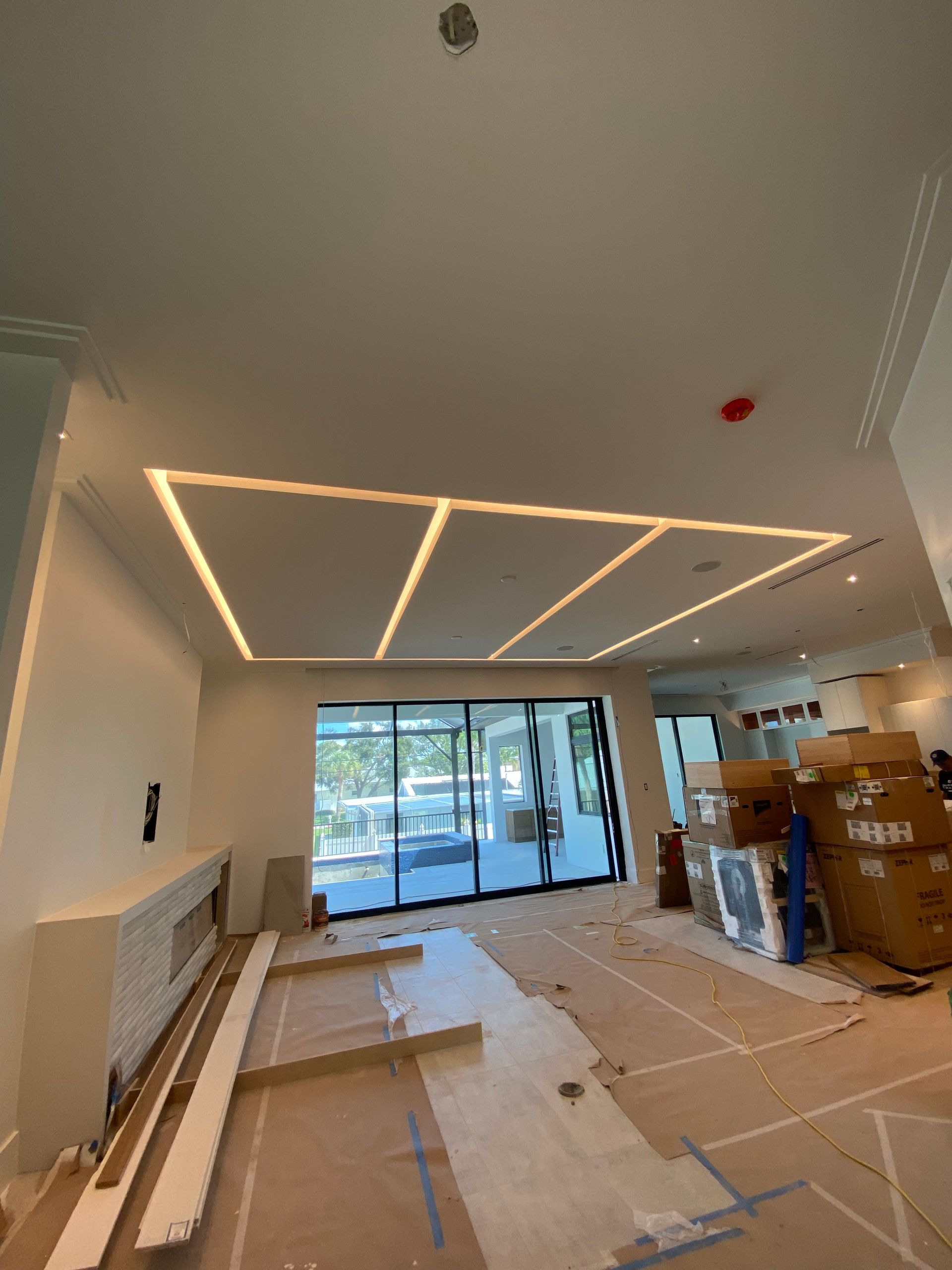 Interior of a modern home under construction; ceiling with recessed lighting, large glass doors, and debris on the floor.
