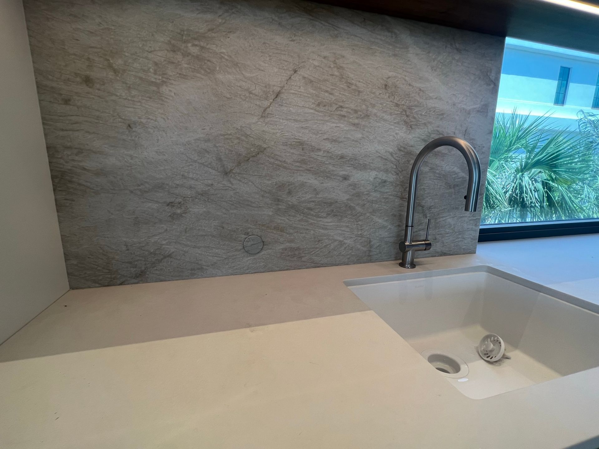Kitchen sink with a stainless steel faucet set against a textured gray backsplash and a white countertop.