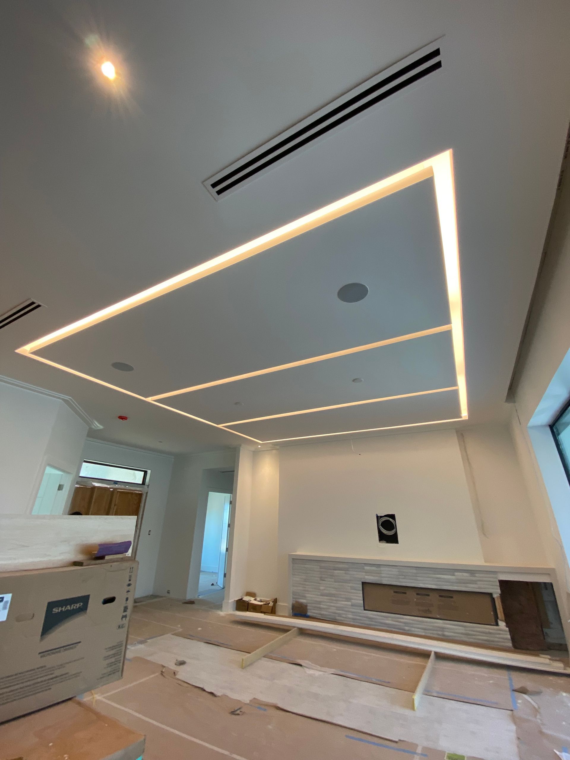 Modern room with recessed lighting in ceiling. White walls, fireplace, and unfinished flooring.