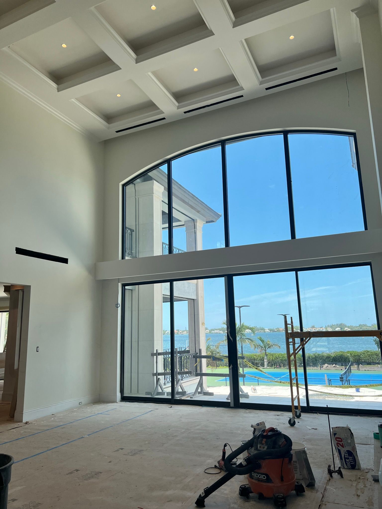 Interior of a house under construction with large arched windows overlooking a pool and the ocean.