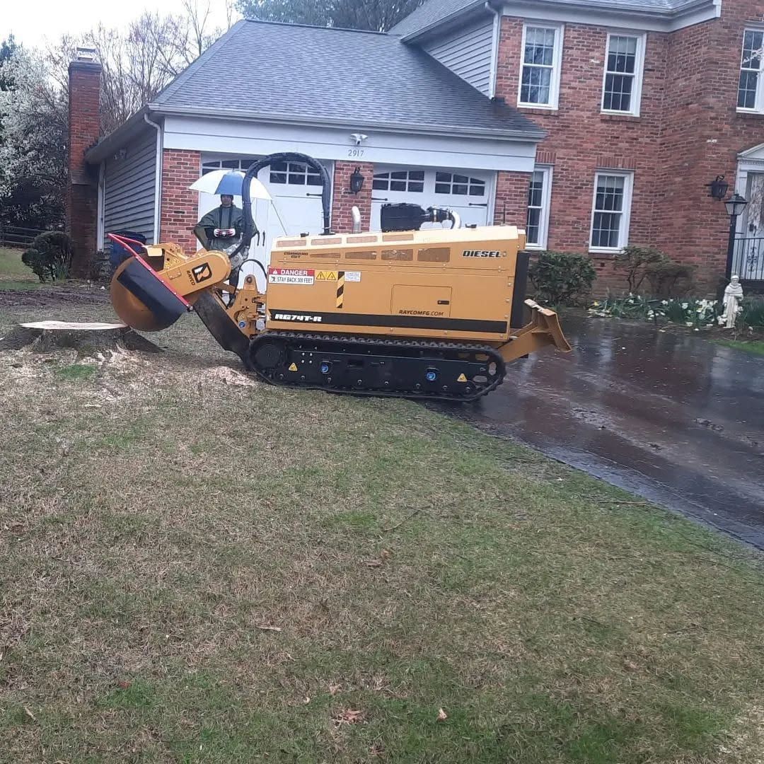 Yellow trenching machine in a wet driveway beside a brick house, with debris piled at the front.