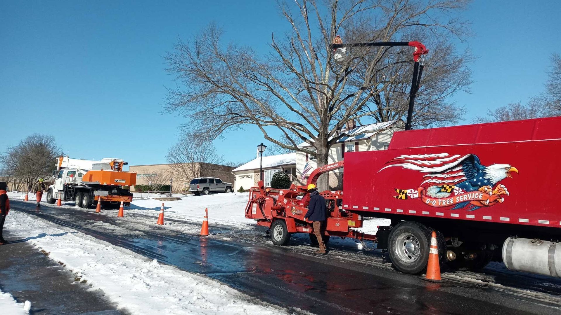 Utility crew and red service trucks working along a snowy roadside with traffic cones.