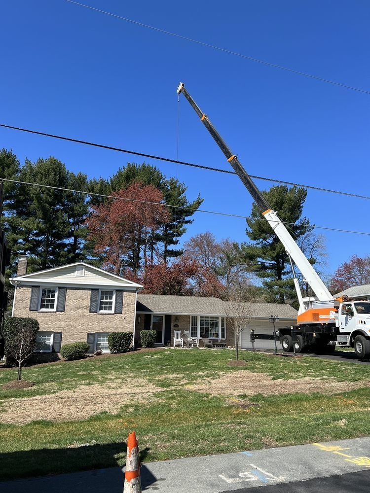 Crane truck lifting a long boom over a suburban house on a sunny day with a clear blue sky.