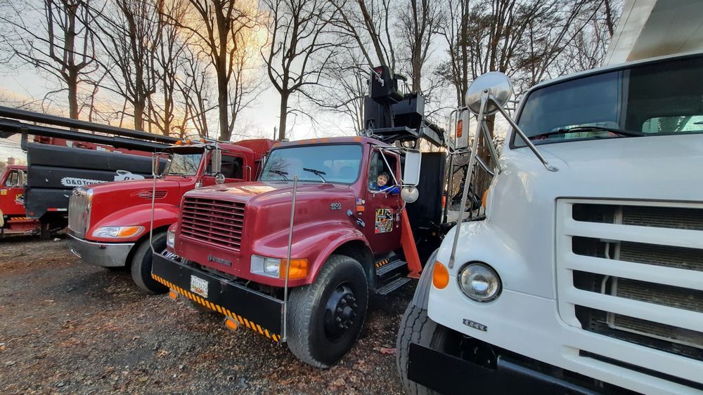Red tow truck parked beside a white truck and red vehicle in a gravel lot at sunset