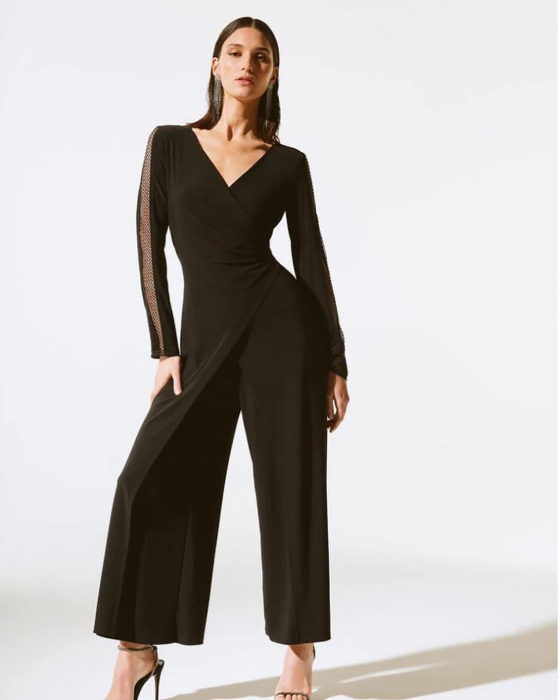 A woman is wearing a black jumpsuit and heels
