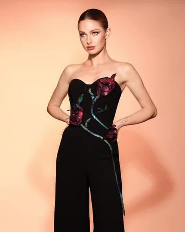 A woman is wearing a black strapless jumpsuit with flowers on it