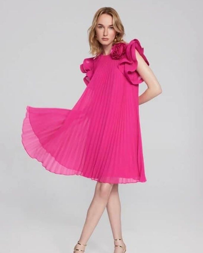 A woman is wearing a pink pleated dress with ruffled sleeves
