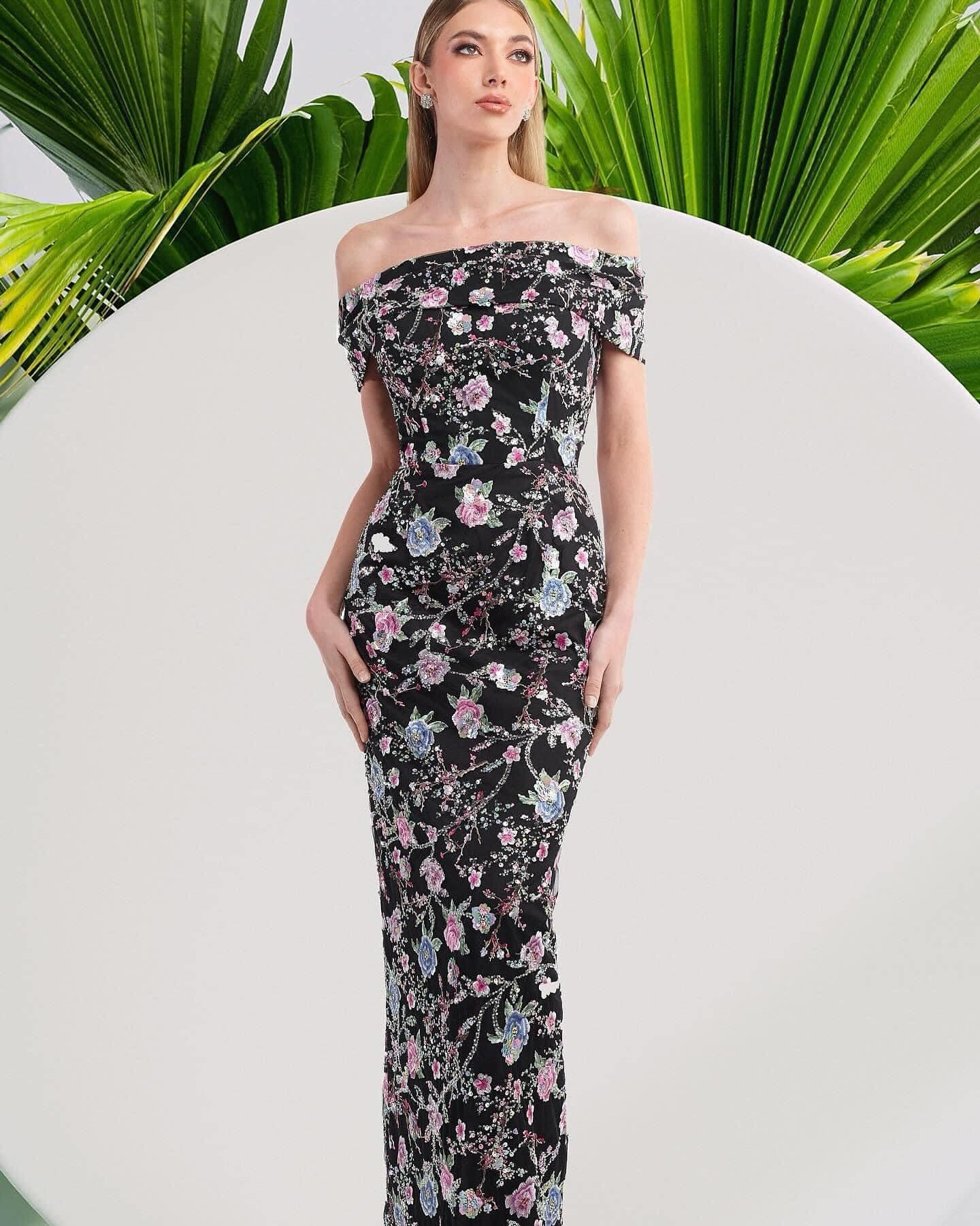 A woman is wearing a black floral off the shoulder dress.