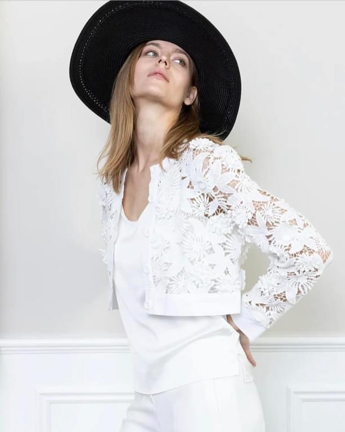 A woman wearing a black hat and a white lace jacket.