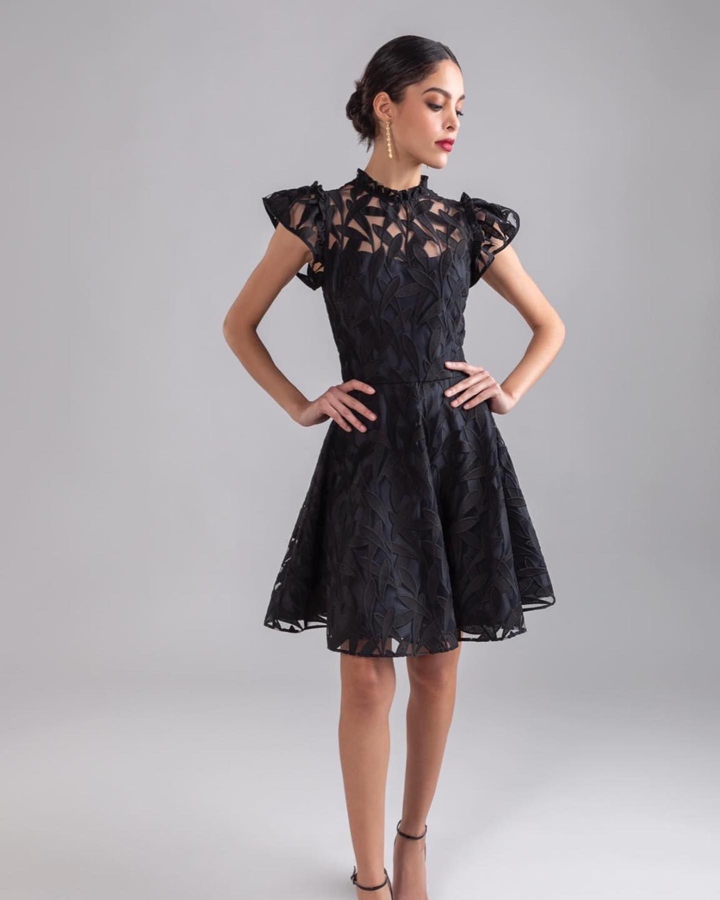 A woman in a black lace dress is standing with her hands on her hips