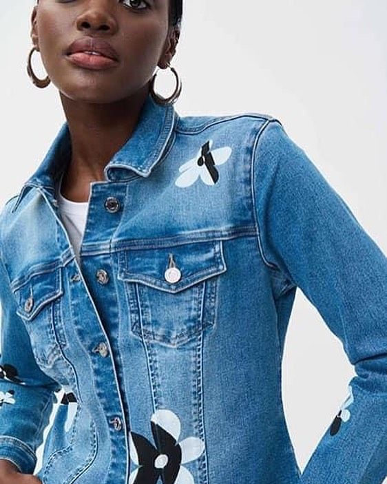 A woman is wearing a blue denim jacket with black and white flowers on the sleeves.