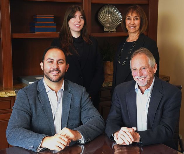 Four people posing in an office, with two seated at a table and two standing behind them.