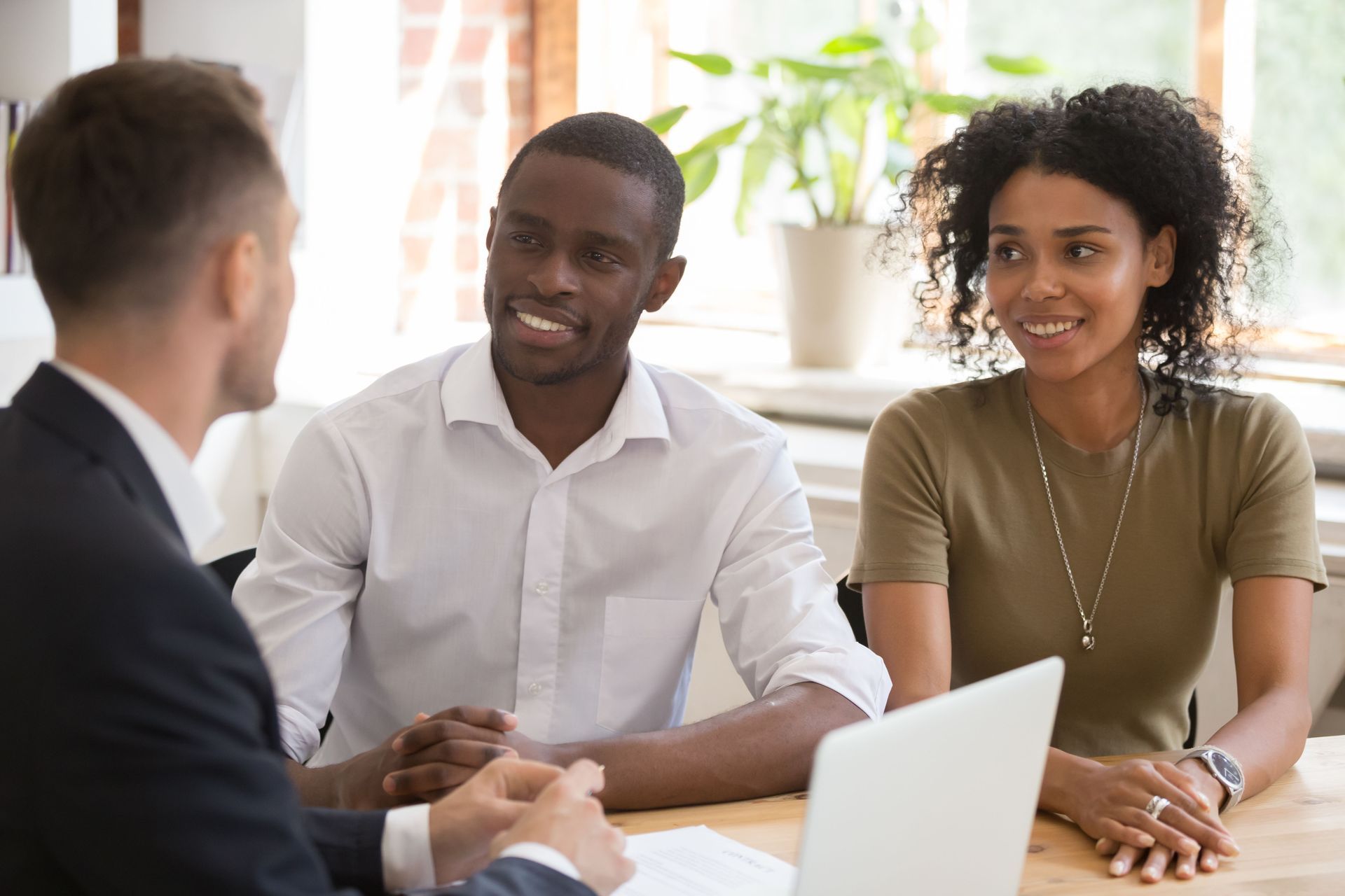 Three people in a meeting with a laptop, smiling at each other in a bright office